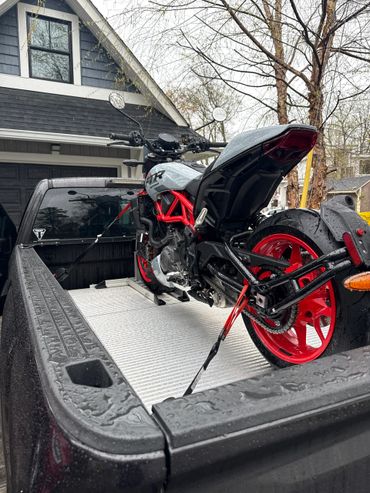 A motorcycle secured in a pickup truck bed on a rainy day to transport to dealer for repair
