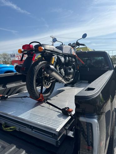 Classic motorcycle secured on a truck bed under a clear sky.