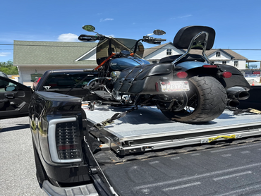 A motorcycle secured in the bed of a black pickup truck on a sunny day.