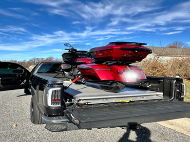 Red motorcycle strapped in the back of a black pickup truck under a clear blue sky.