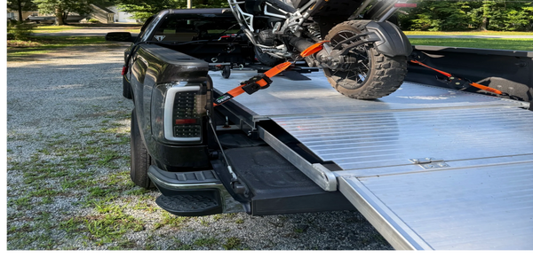 Motorcycle secured on a truck bed ramp with orange straps on a sunny day.