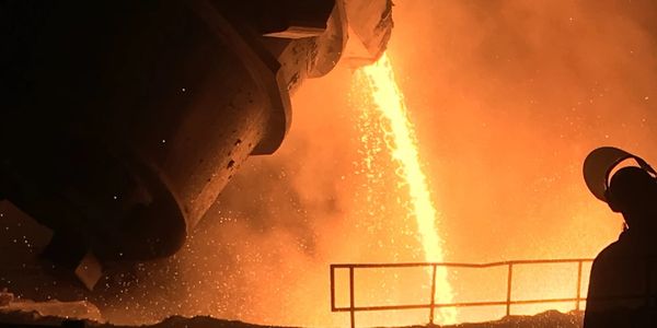 Molten metal pouring from a large industrial ladle in a steel factory.