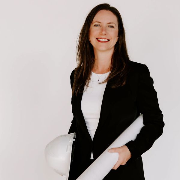 Woman smiling wearing a suit and carrying a hard hat and rolled up construction plans