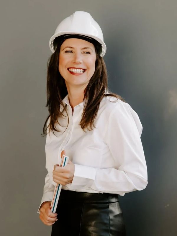 Woman standing and smiling wearing a hard hat and holding an engineering scale ruler
