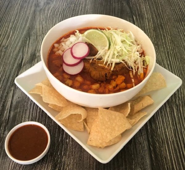 Bowl of soup garnished with lime, radish, and cabbage, served with tortilla chips and salsa.