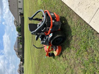 A red zero-turn lawn mower parked on a grassy area near a sidewalk.