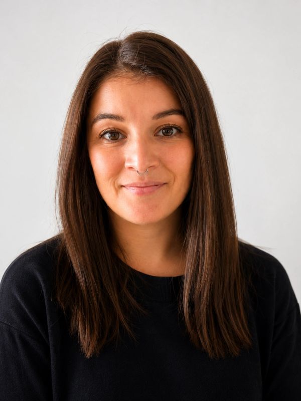 Young woman with long brown hair and septum piercing smiling.