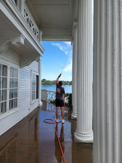 Person cleaning a large porch ceiling with a hose on a sunny day.