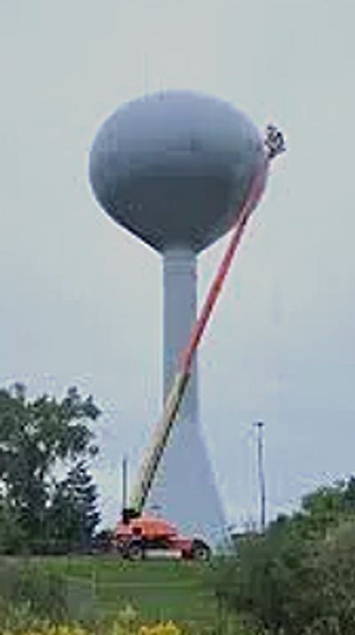 A worker on a lift cleaning a large water tower.