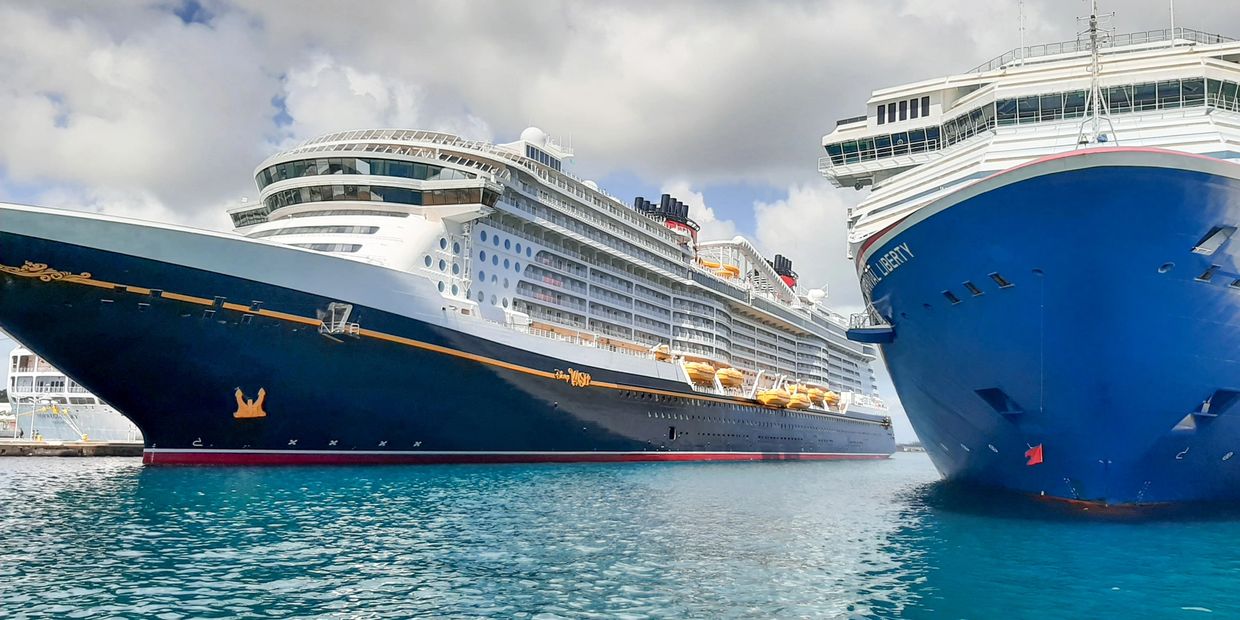 Two large cruise ships docked side by side in clear blue water under a partly cloudy sky.