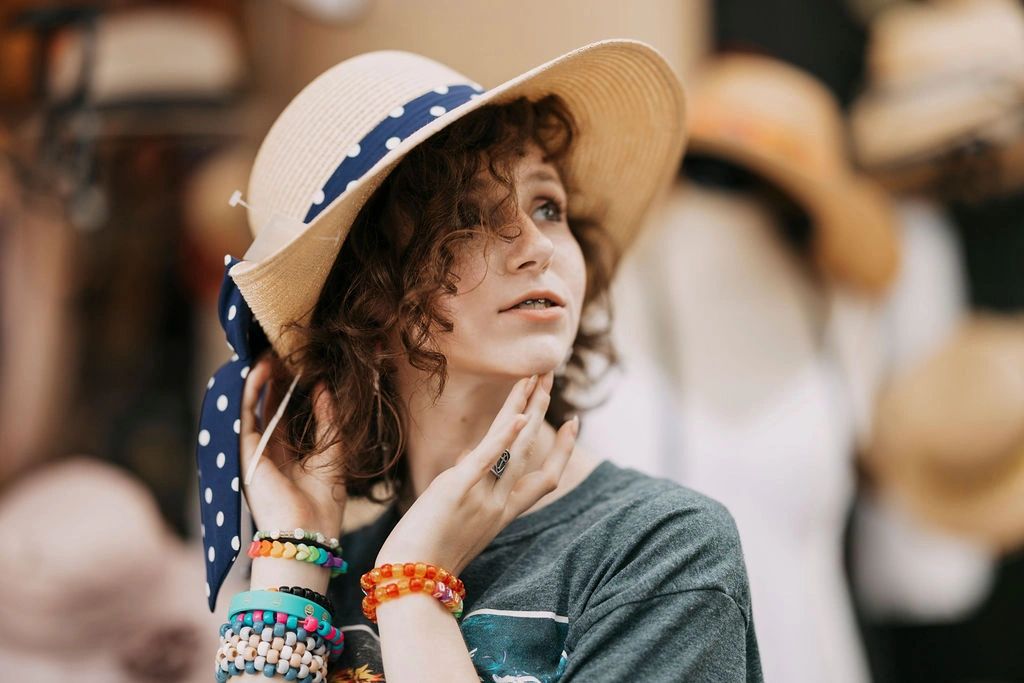 Young woman with curly hair wearing a polka-dot hat and colorful bracelets.