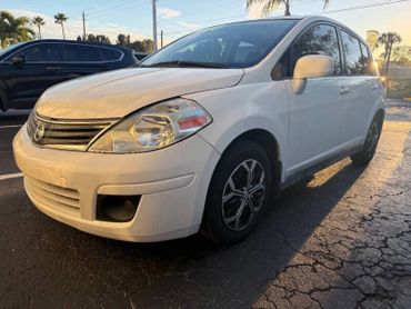 White Nissan hatchback parked on cracked asphalt in sunset light.