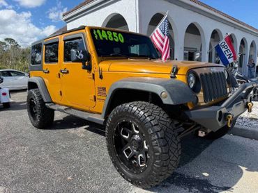 Orange Jeep Wrangler for sale priced at $14,850 with large off-road tires.