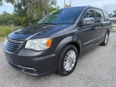 Gray Chrysler minivan parked outdoors near trees and grass.