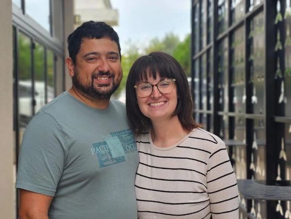 Smiling couple standing close outside a building, enjoying a casual moment together.
