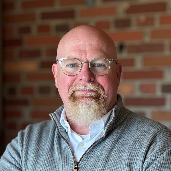 Portrait of a bald man with glasses and a white beard, wearing a gray sweater.