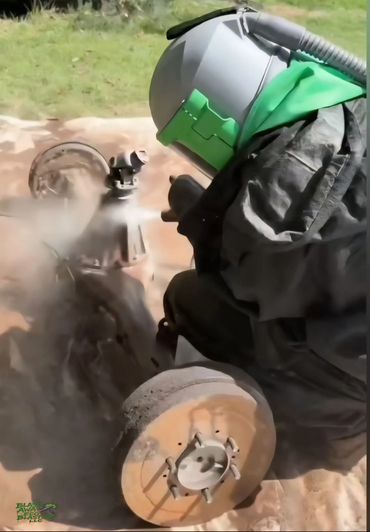 Worker sandblasting a rusty vehicle part outdoors with protective gear.