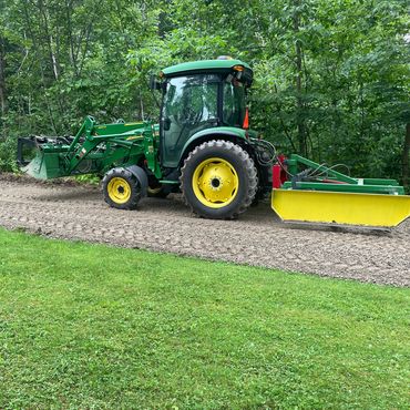 John Deere with a land plane, loader and grapple bucket, on freshly graded gravel driveway.