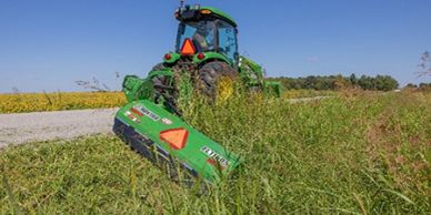 A green tractor mowing tall grass on a sunny day.