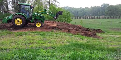 Green tractor digging soil on a farm field.