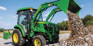 Green tractor with front loader dumping rocks on a gravel road.