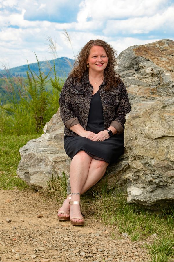 Woman sitting on a large rock outdoors with a scenic mountain backdrop.