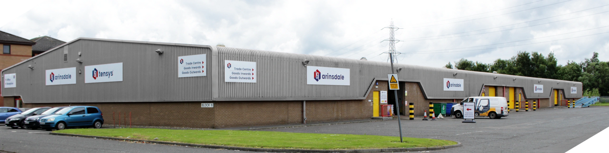 Large industrial building with Arinsdale and Tensys logos and parked cars.