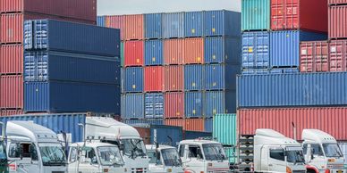 Stacked shipping containers and trucks representing logistics and global trade.