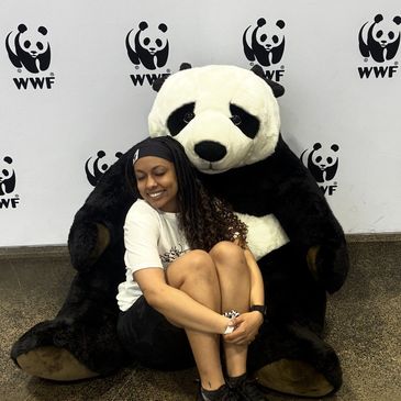 A woman happily posing with a giant panda mascot at WWF event.