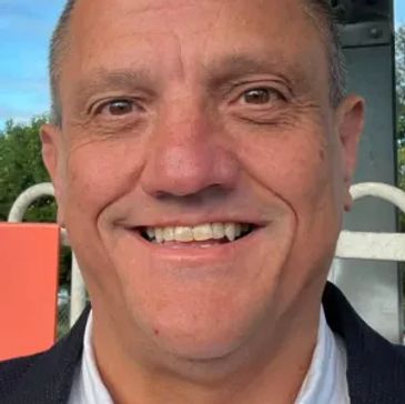 Smiling man in a white shirt and dark jacket outdoors.