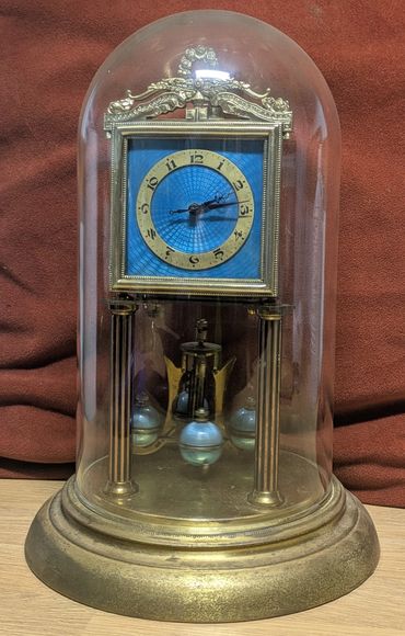 Vintage anniversary clock with blue face under glass dome.