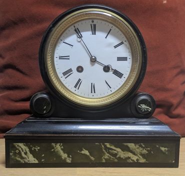 Antique black mantel clock with Roman numerals and marble accents.