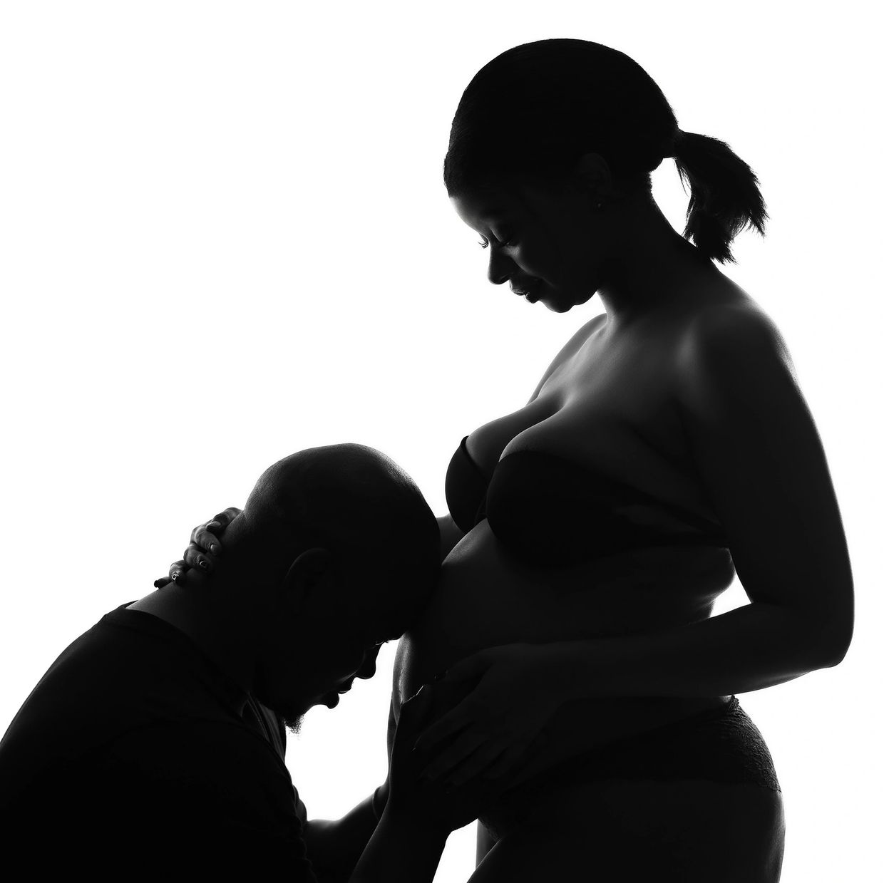 Silhouette of a man kissing a pregnant woman's belly.