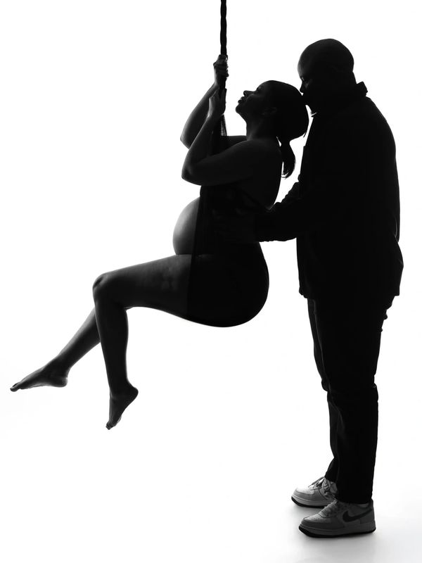 Silhouette of a pregnant woman on a swing with a man supporting her.