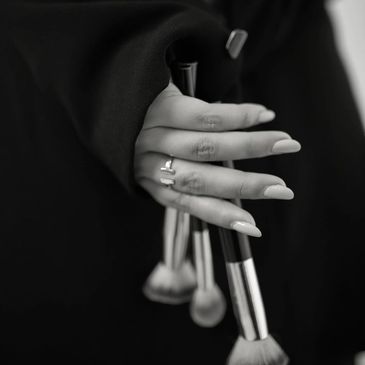 Hand with rings holding makeup brushes in black and white.