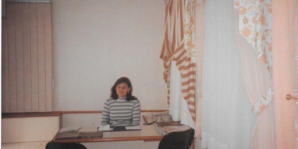 Uma mulher (Irene Ruppel) sentada em uma mesa de escritório. 