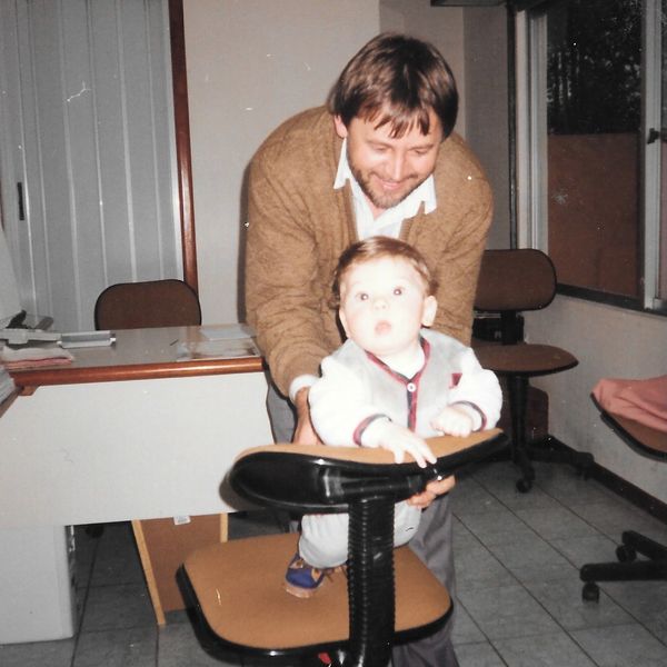 Homem (Nelson Ruppel) brincando com o filho em uma cadeira na loja Condor Cortinas do Bigorrilho.
