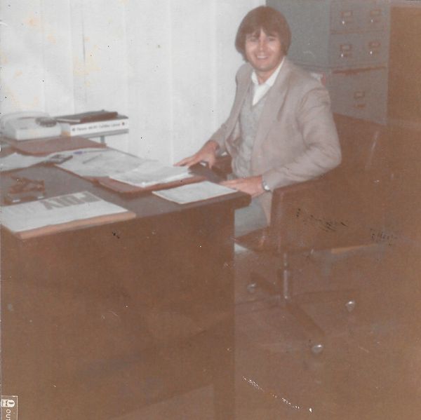 Homem (Nelson Ruppel) sentado em frente a uma mesa de escritório. Loja Condor Cortinas Curitiba.