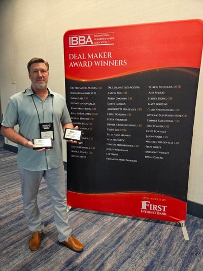 Man holding awards next to Deal Maker Award Winners board.