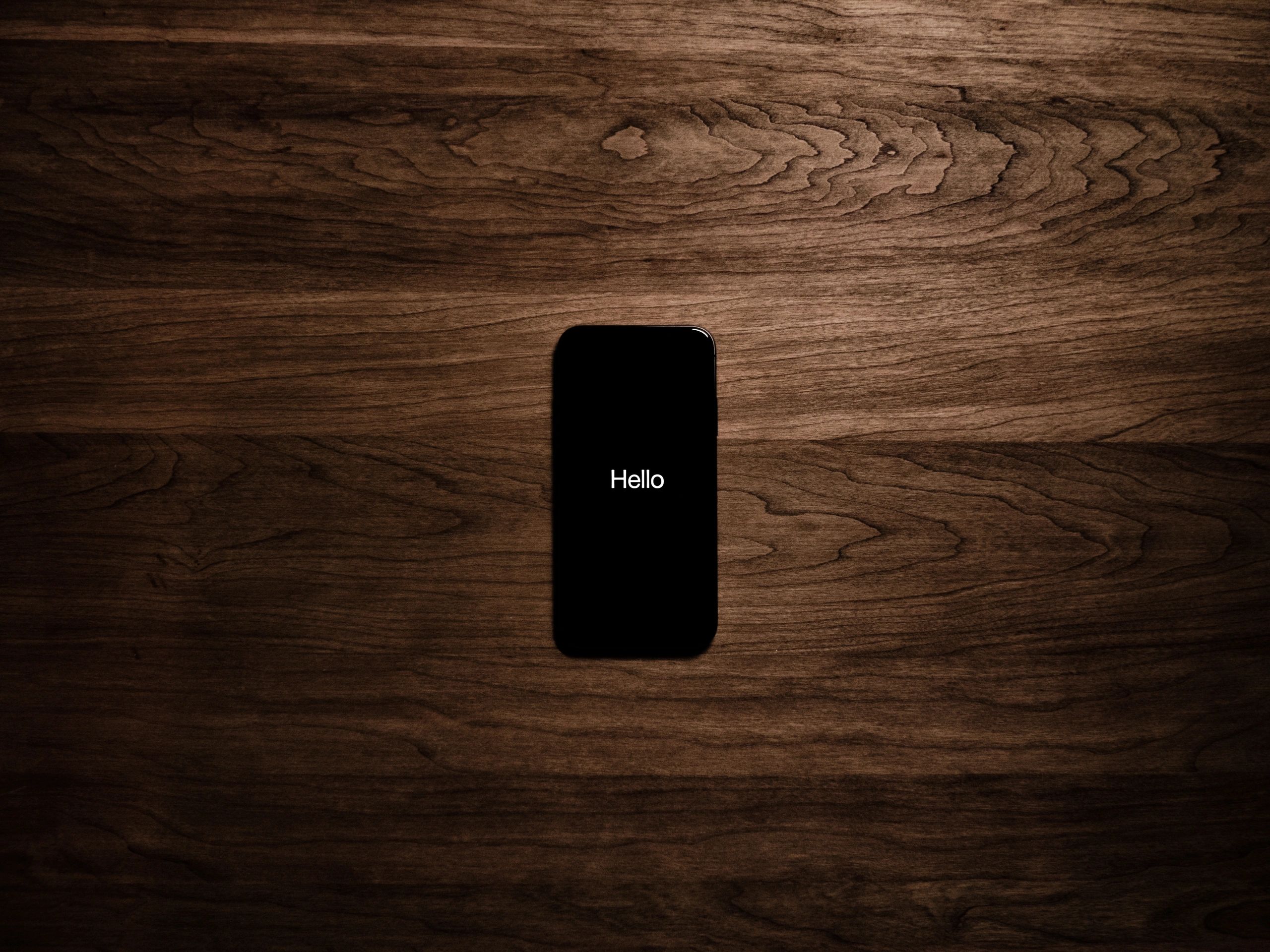 picture of a cell phone on a wooden background. The cell phone screen says "Hello"