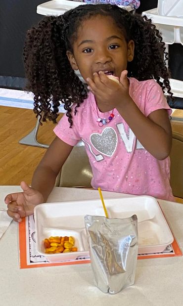 Young girl eating snack at a table with juice pouch and crackers.