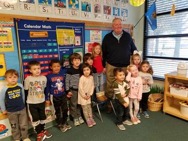 Teacher poses with a group of young students in a colorful classroom.