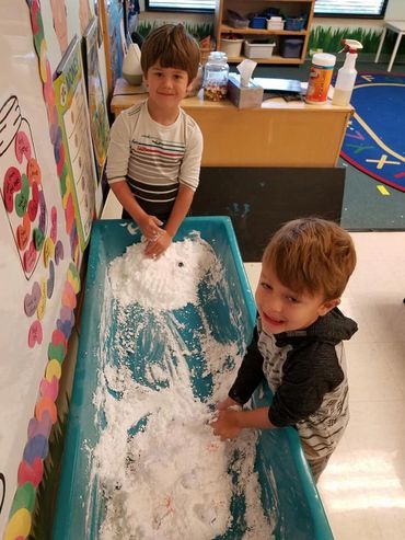 Two boys playing with white sensory material in a classroom tub.