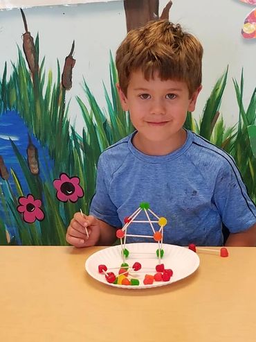 Boy building a structure with toothpicks and candy on a plate.