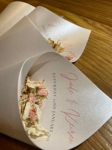 Paper Confetti Cones lay on a wooden table, filled with pink and white, dried, petal confetti.