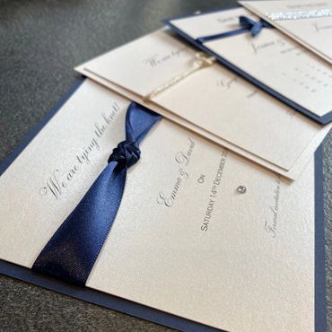 White, Save the Date Invitation with navy blue ribbon and diamond embellishment.