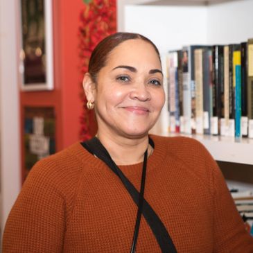 a 40s or 50s person of color, smiling no teeth, wearing a deep orange sweater