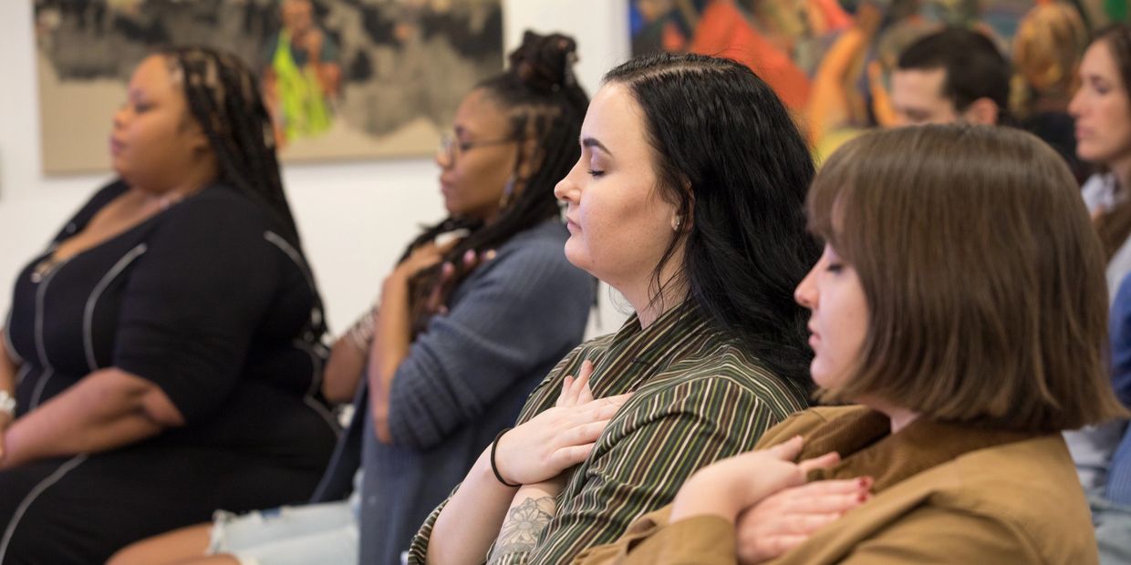 people sitting in a room, with eyes closed, and hands to their hearts