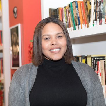 young black woman, with straightened hair to her shoulders, wearing a cardigan and black turtleneck