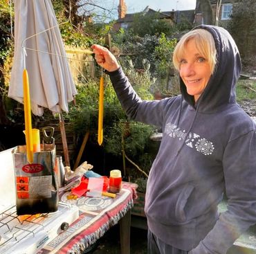 Jane Horrocks is holding a wire hanger that has two candles hanging from it after candle-dipping